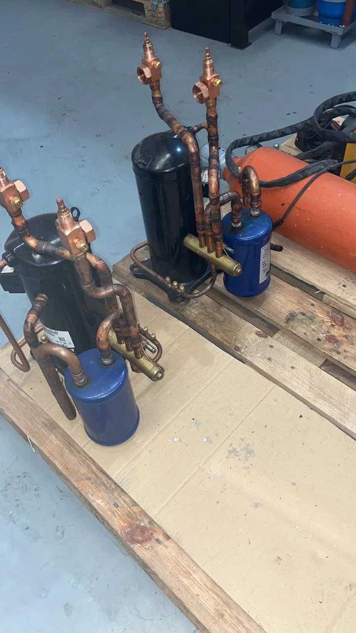 Sistema de refrigeración con compresores y tubos de cobre sobre una estructura de madera.