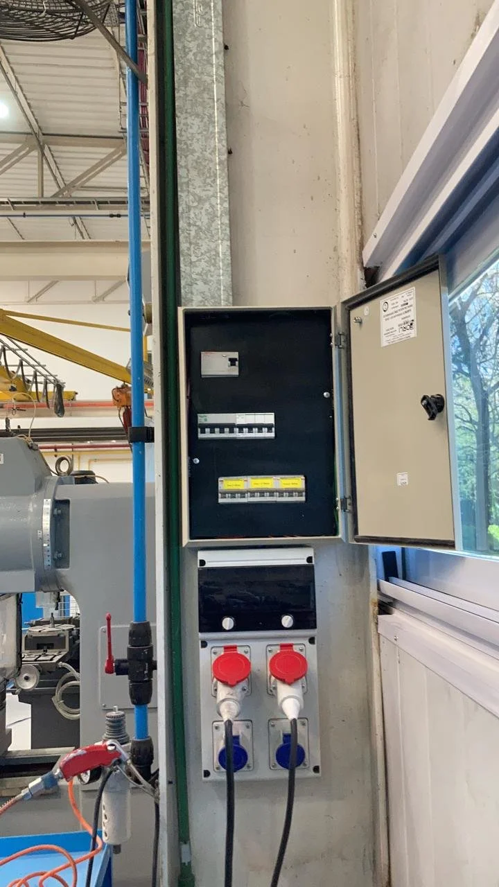 Panel de control eléctrico con interruptores, enchufes y cables en un entorno industrial.