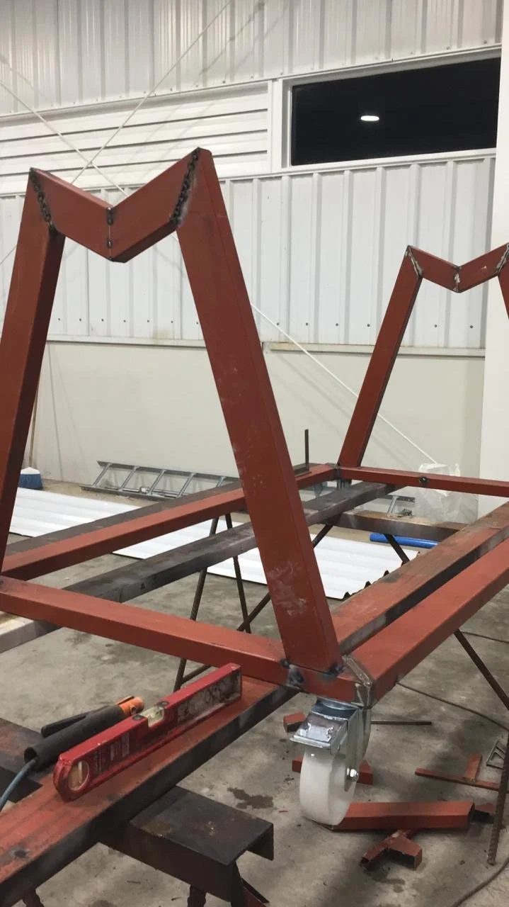Estructura metálica rosa en proceso de ensamblaje en un taller, con ruedas y herramientas en el suelo.