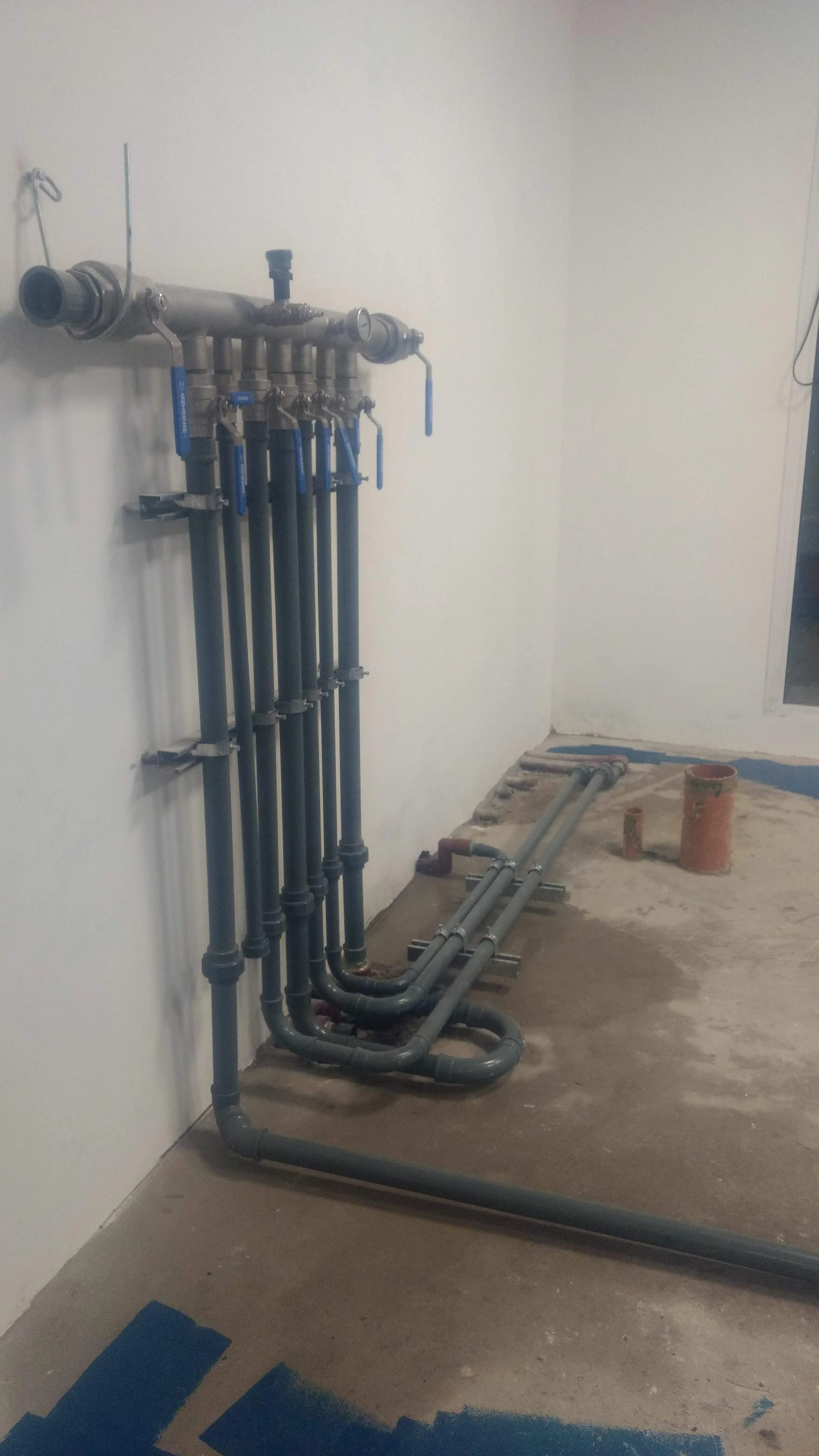 Tuberías de plomería instaladas en una pared y suelo de cemento en construcción o remodelación.