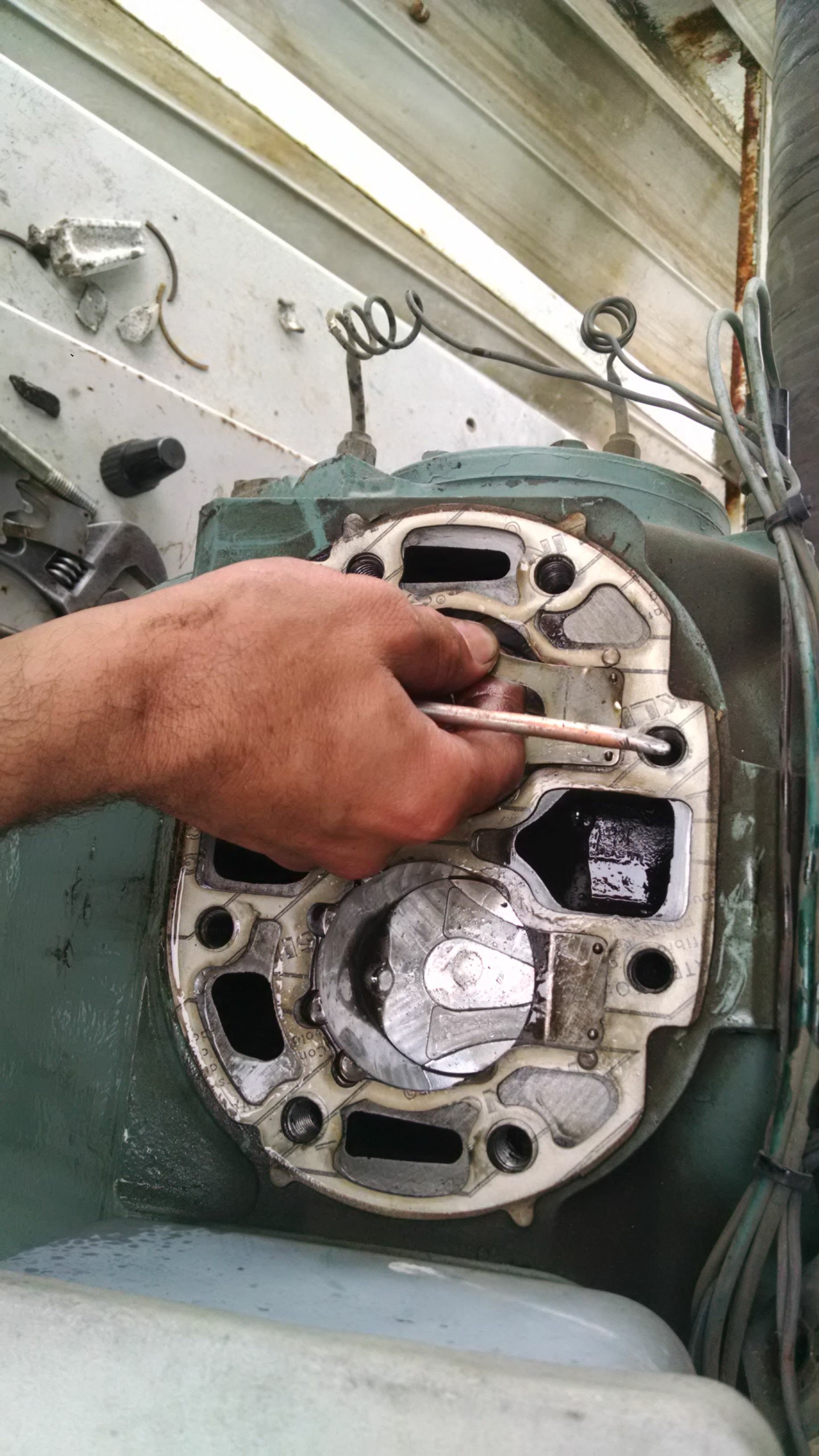 Mano trabajando en la cabeza de un motor de automóvil, usando una herramienta para ajustar o reparar.