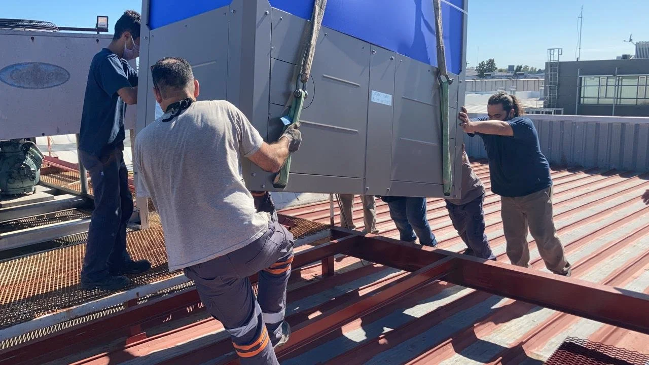 Varias personas trabajando juntas para mover una gran unidad en el techo de un edificio.