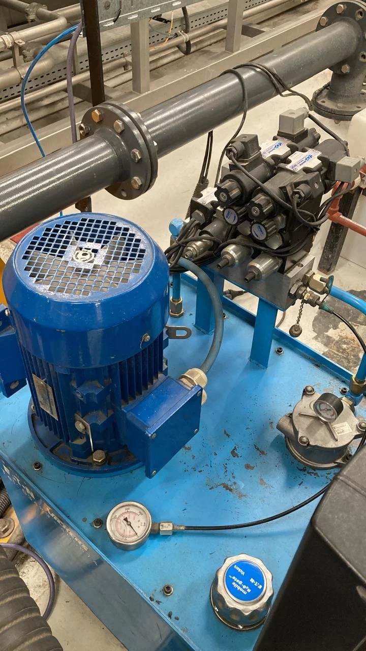 Sistema de bombeo con motor azul, tuberías, manómetro y componentes eléctricos en una instalación industrial.