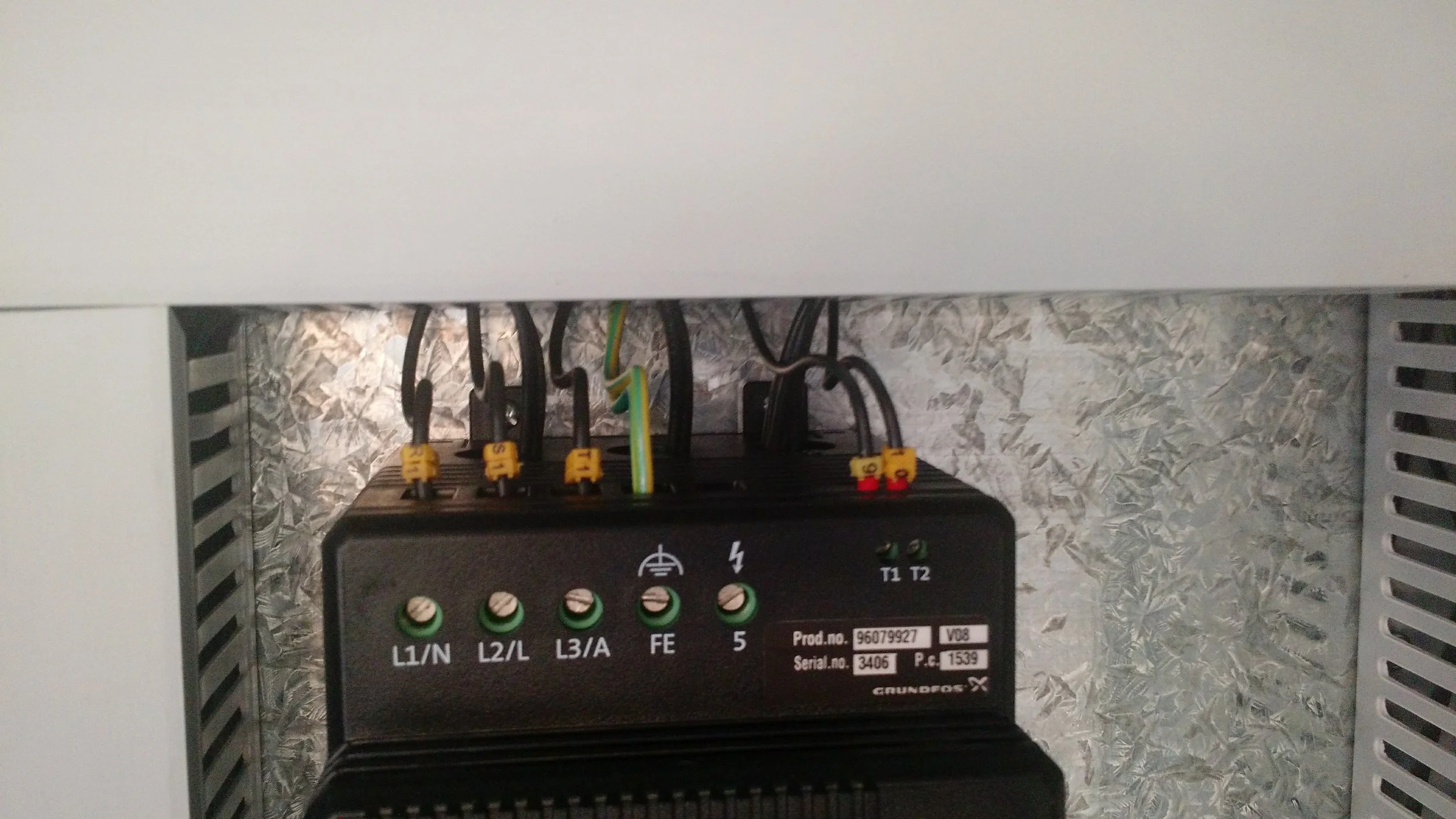 Caja de componentes eléctricos en una caja de distribución con cables y conectores visibles en un fondo de paredes de mosaico de piedra.