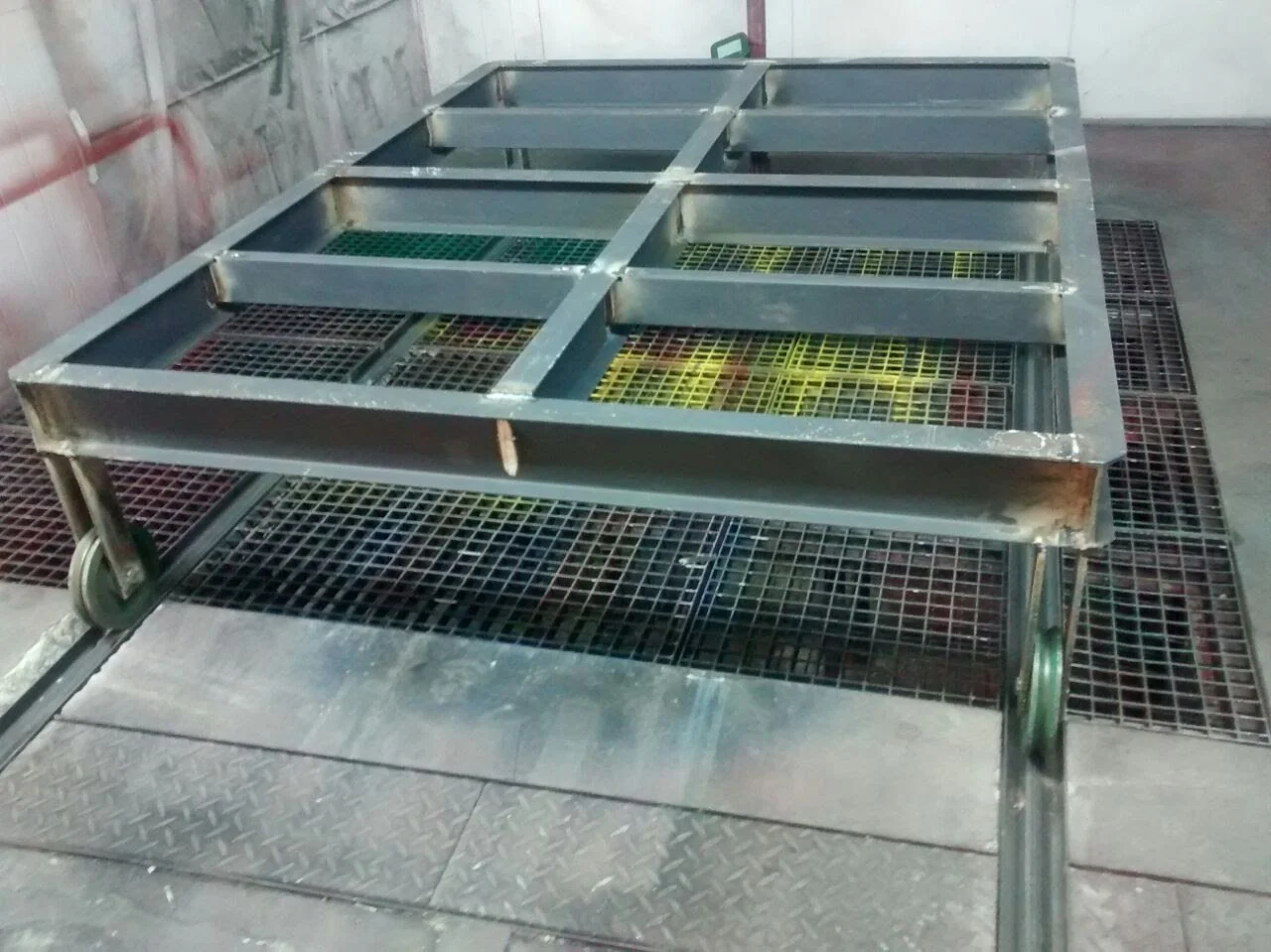 Estructura metálica en un taller de fabricación con ruedas en las patas y rejillas en la parte superior, posiblemente utilizada para soporte o transporte de objetos.