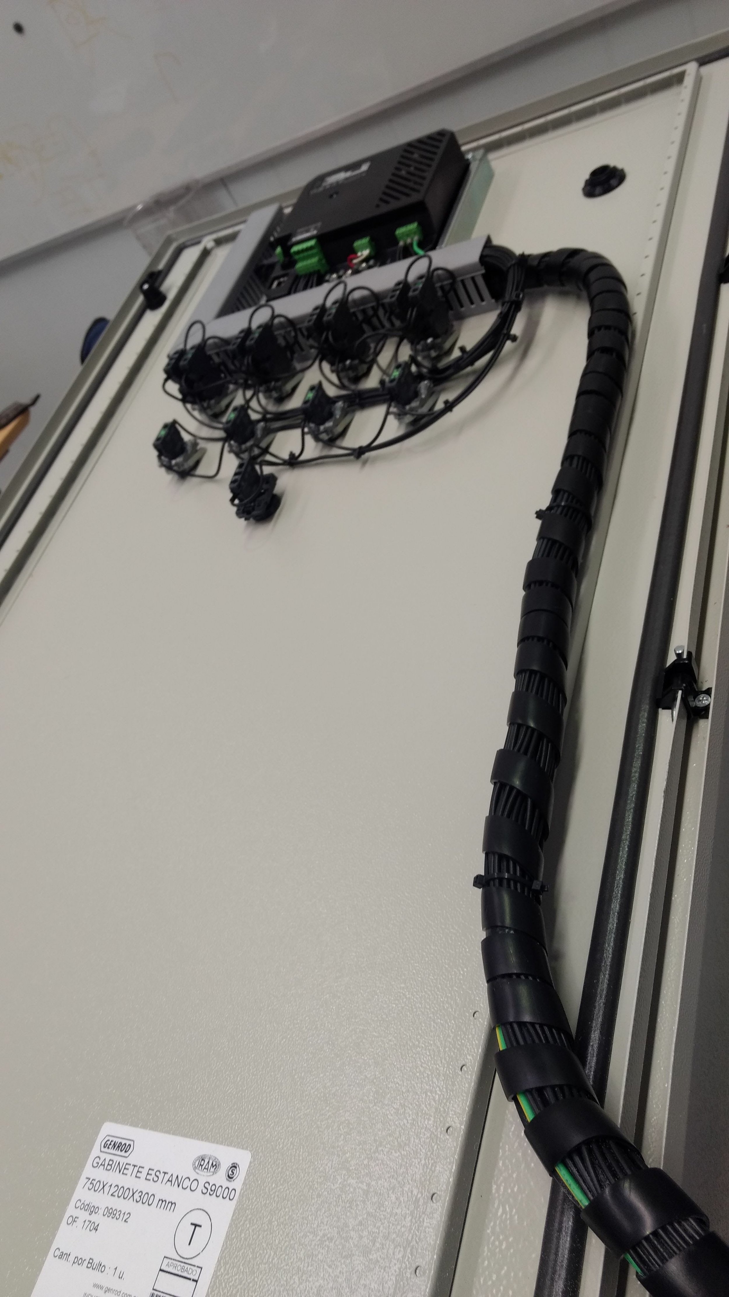 Conjunto de cables eléctricos organizados en una bandeja sobre una pared, conectado a una caja de distribución eléctrica en una oficina o espacio técnico.
