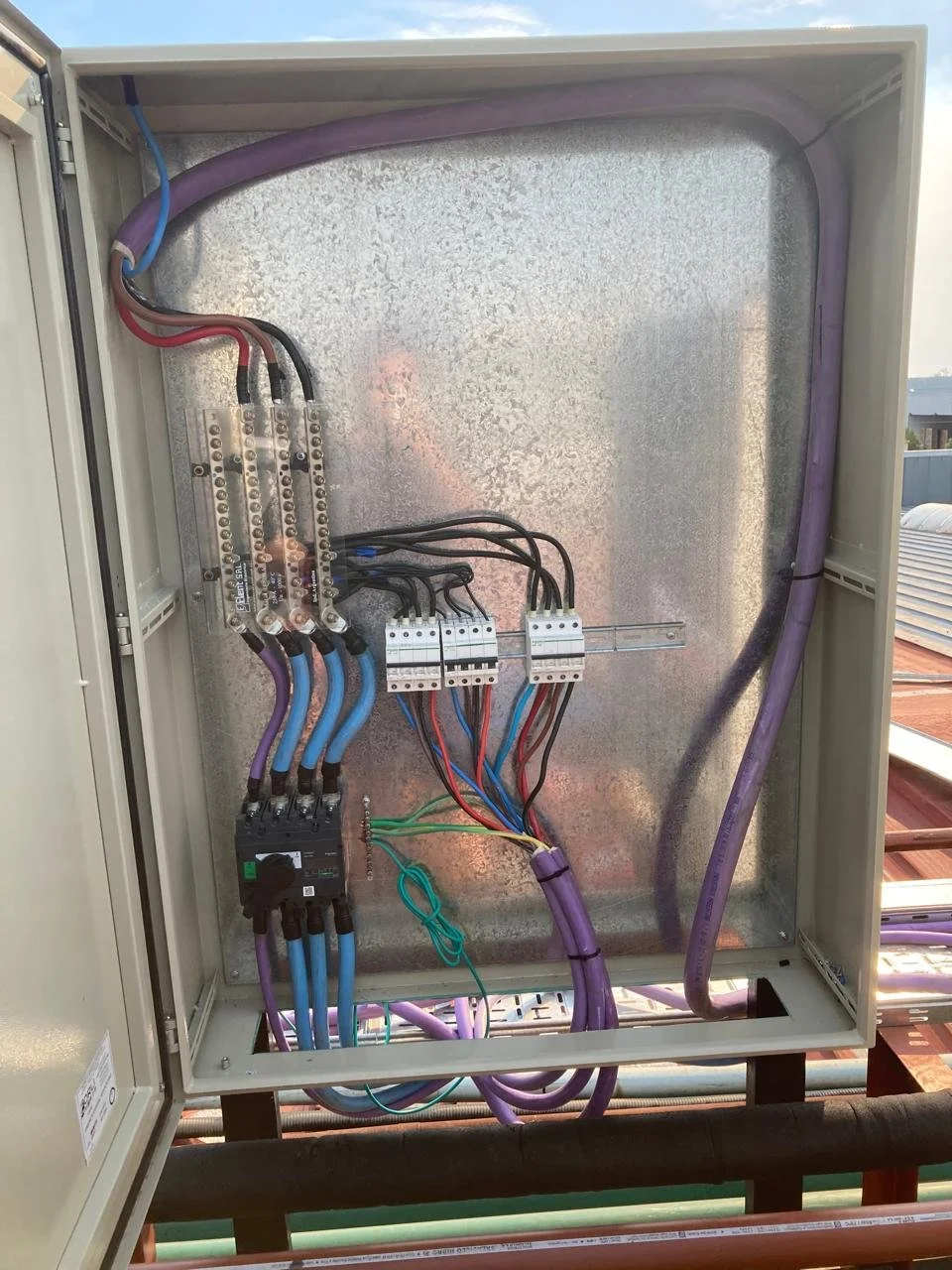 Caja de conexiones eléctricas con cables de colores y componentes metálicos, algunos cables están agrupados con ataduras.