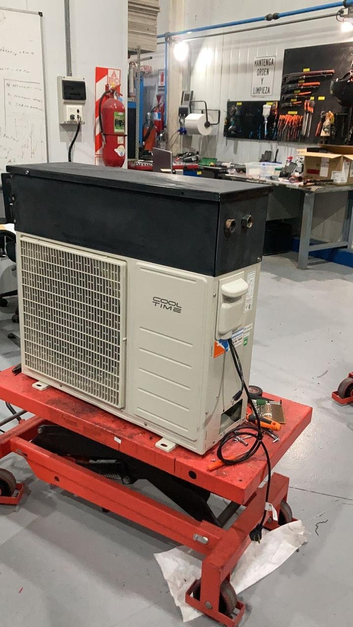Una unidad de aire acondicionado o refrigeración en proceso de reparación en un taller, sobre una plataforma con herramientas y piezas alrededor.