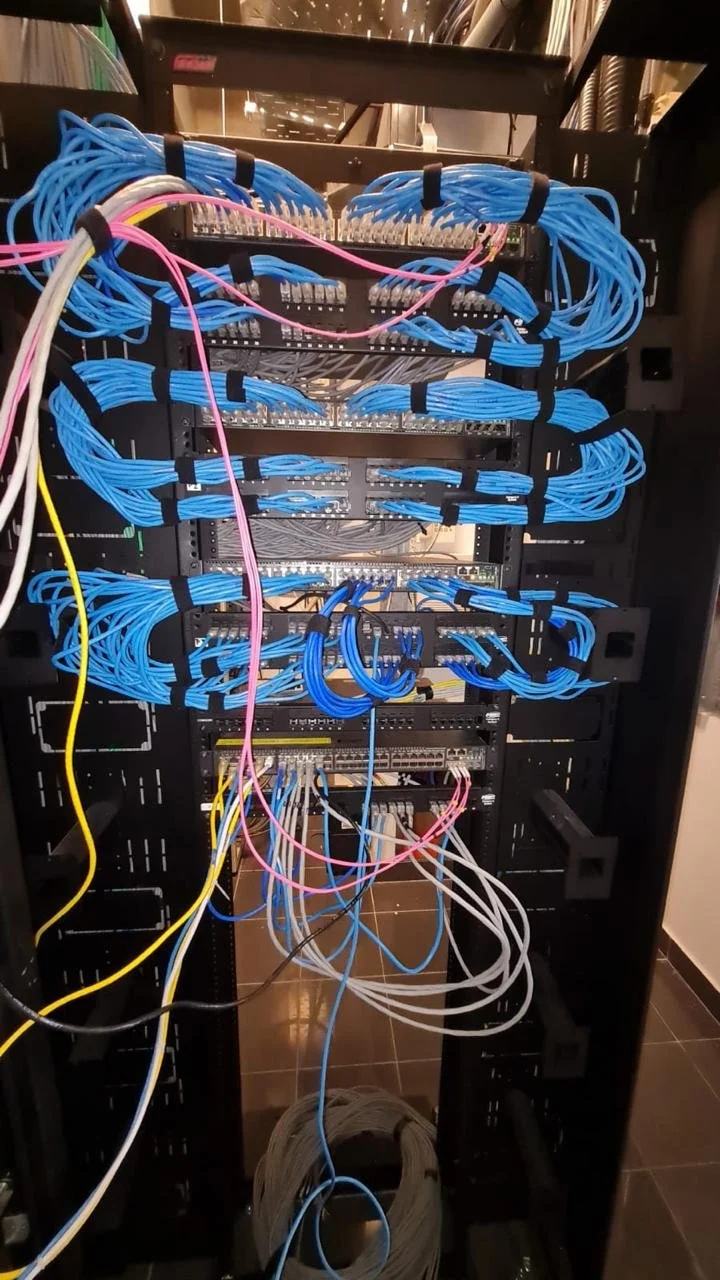 Armario con cableado de red organizado, con cables azules, blancos, amarillos y rosados conectados a equipos de red.