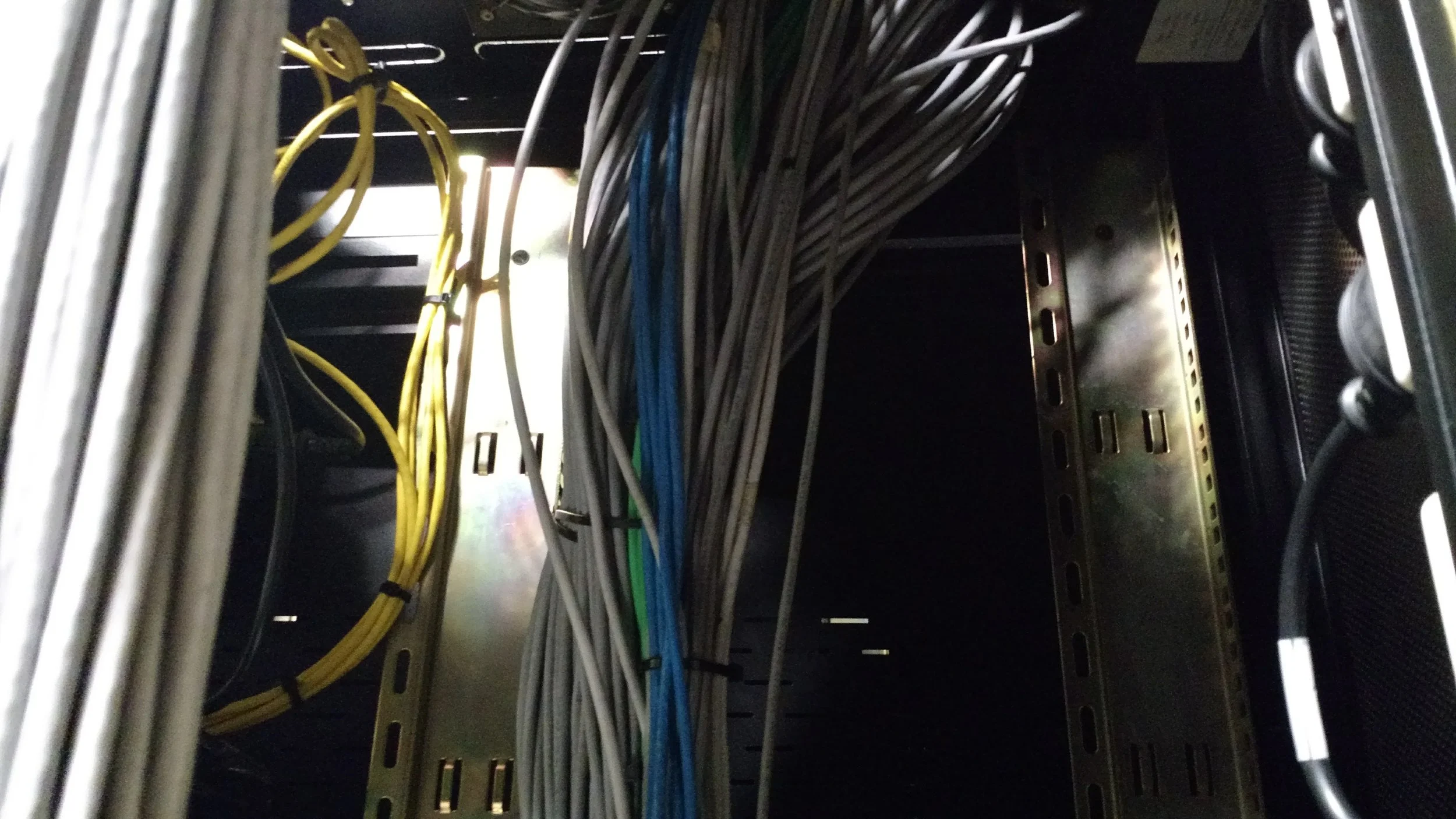 Panel de cableado en un armario de servidores con cables de diferentes colores y una estructura metálica.