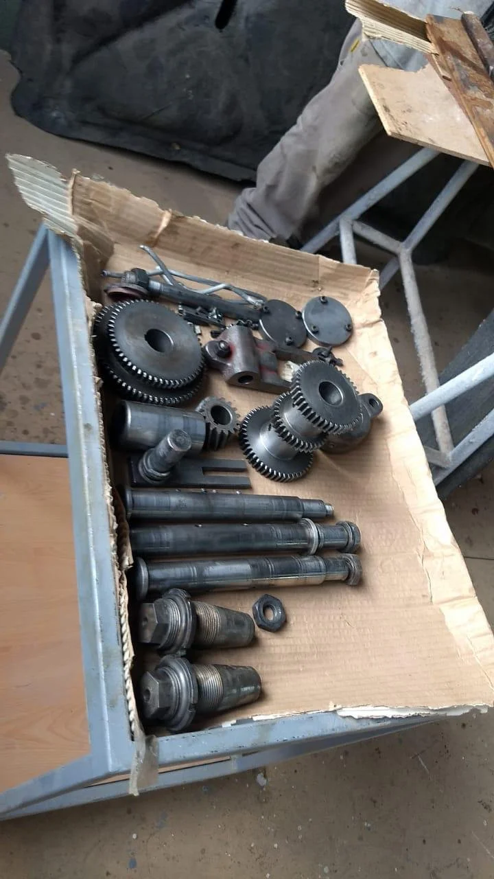 Conjunto de engranajes, ejes y piezas metálicas en una caja de cartón, en un taller mecánico.