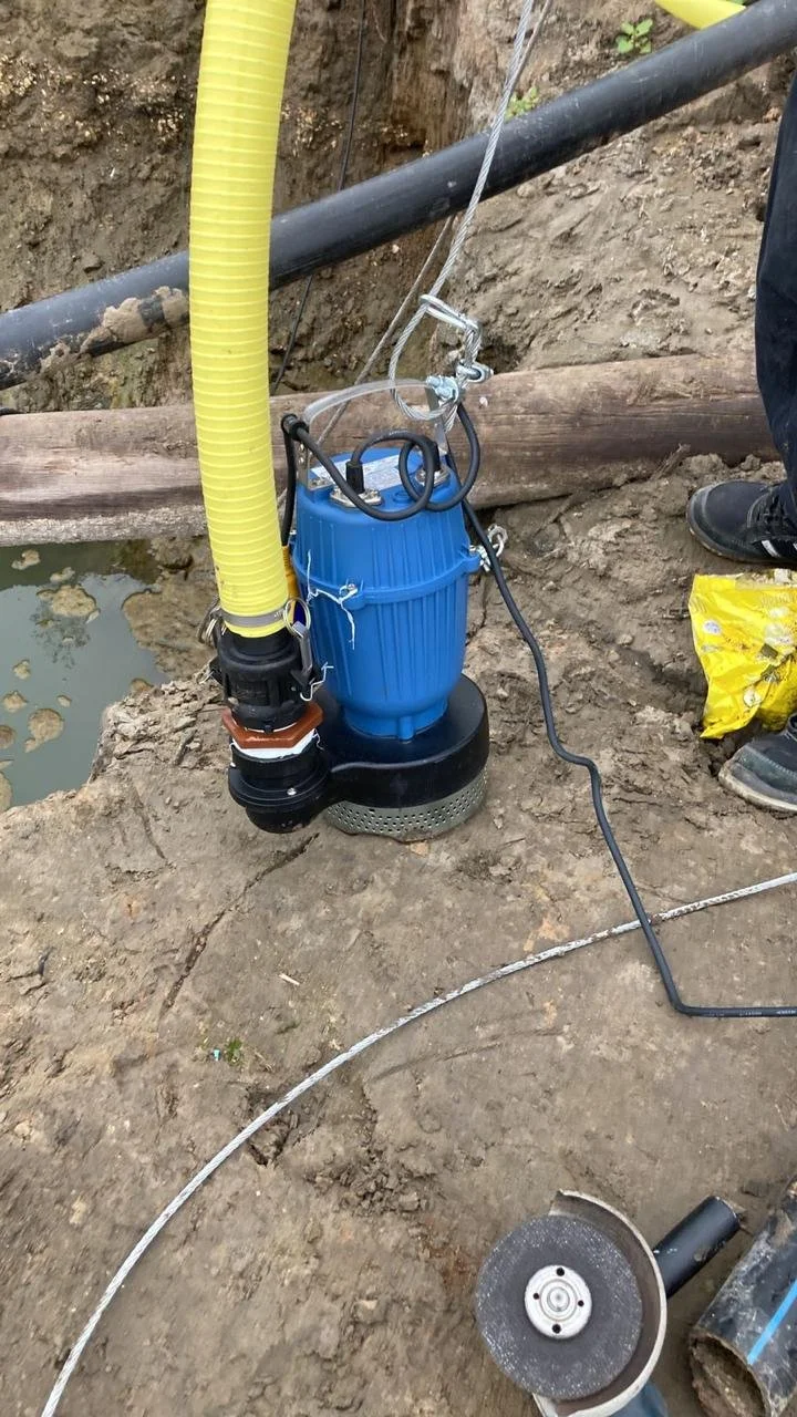 La imagen muestra una maquinaria de bomba sumergible en un trabajo de excavación, con tuberías y arena en un sitio de construcción.