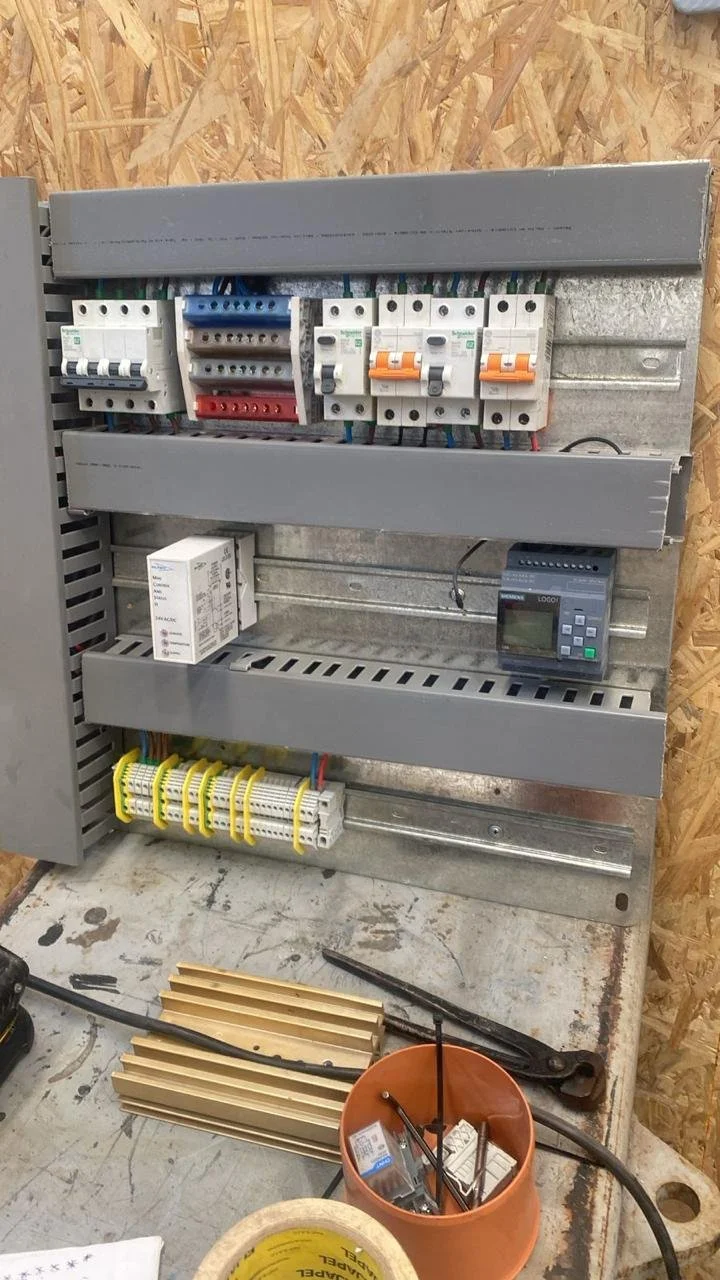 Cuadro eléctrico con componentes eléctricos, incluyendo disyuntores y un temporizador en un taller de reparación.