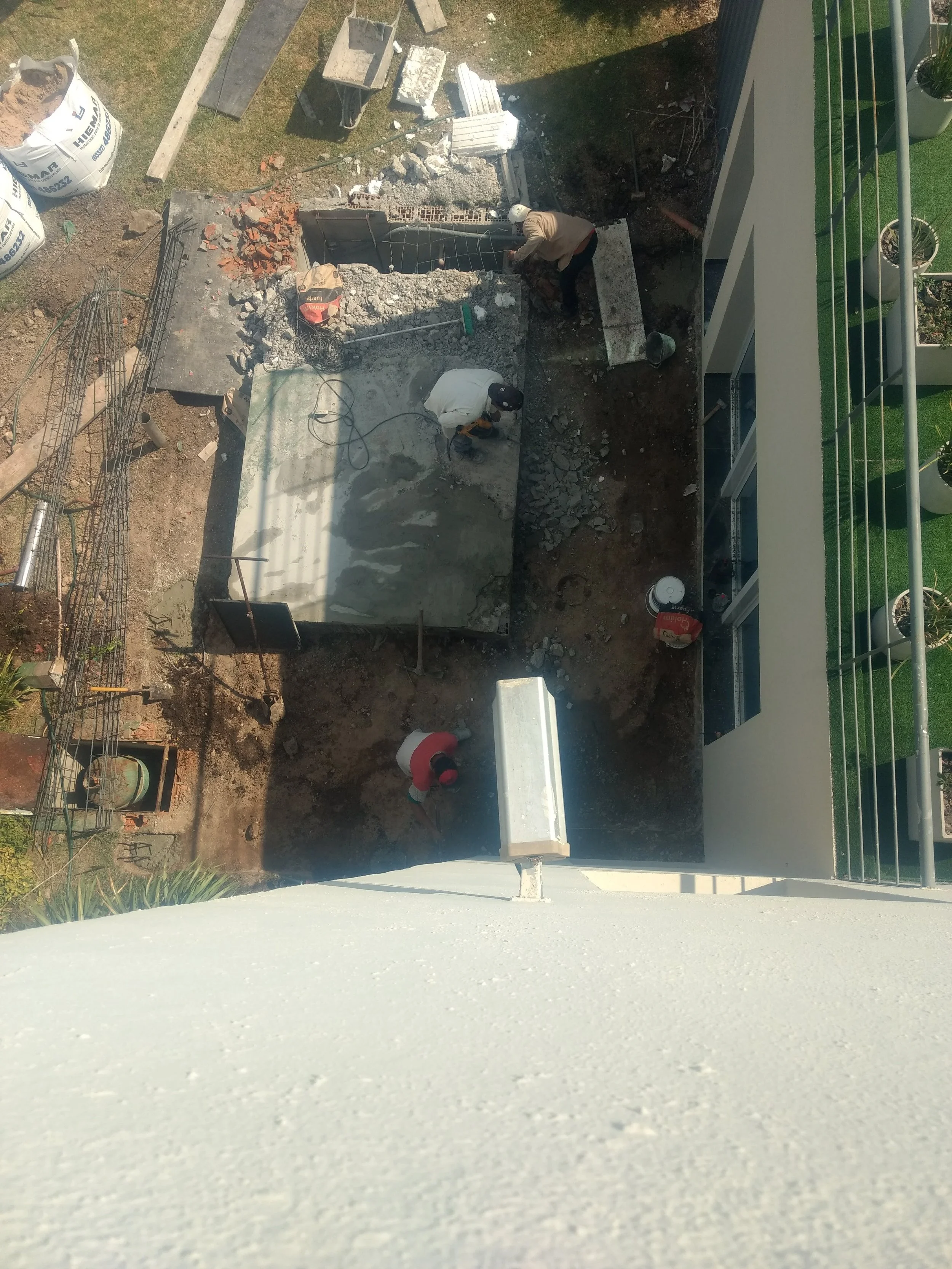 Dos trabajadores realizando trabajos de construcción o demolición en un área de terreno con maquinaria y material de construcción.