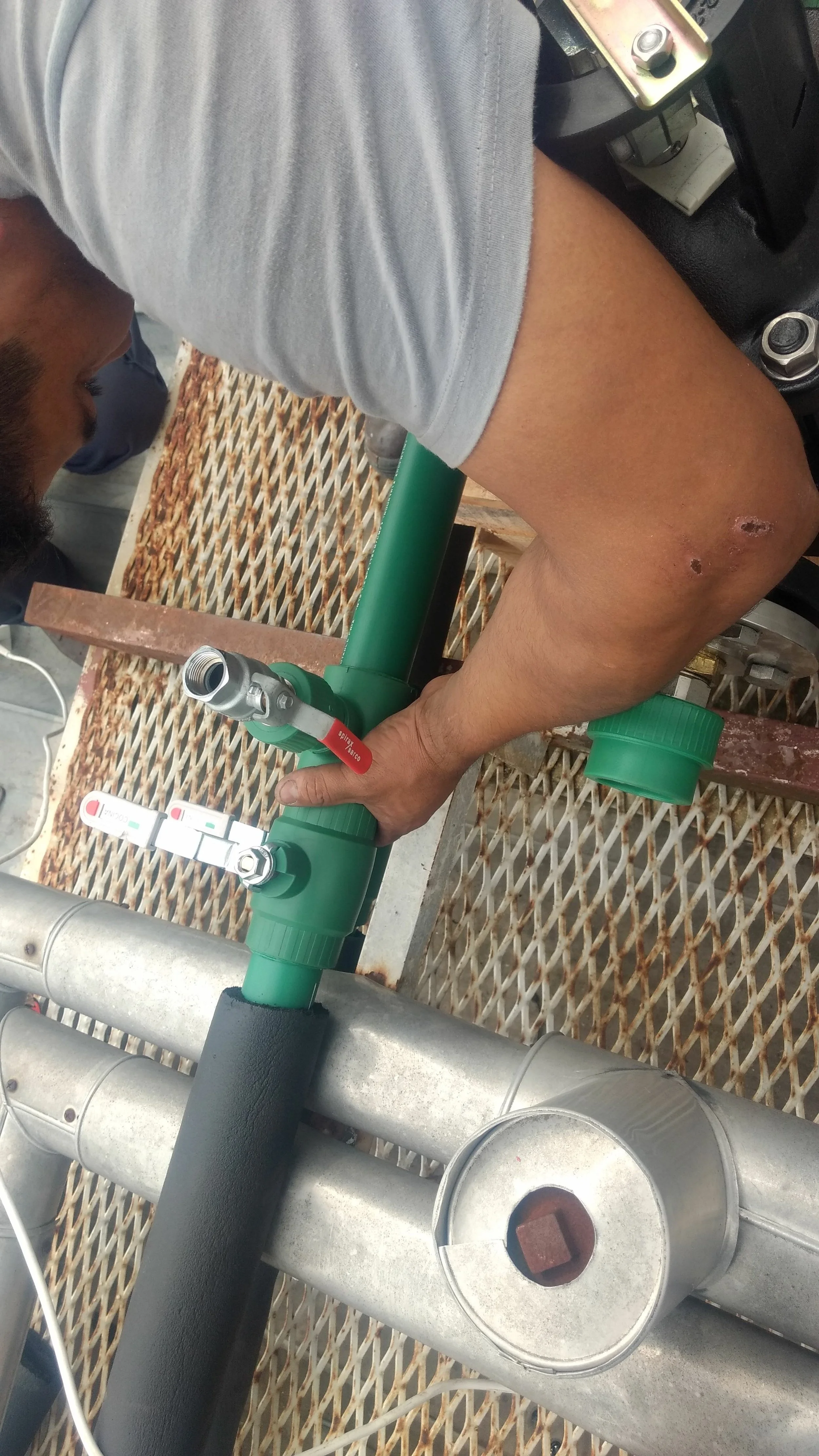 Hombre trabajando en sistema de tuberías, ajustando válvula en tubería de metal y plástico en un entorno de construcción o ingeniería.