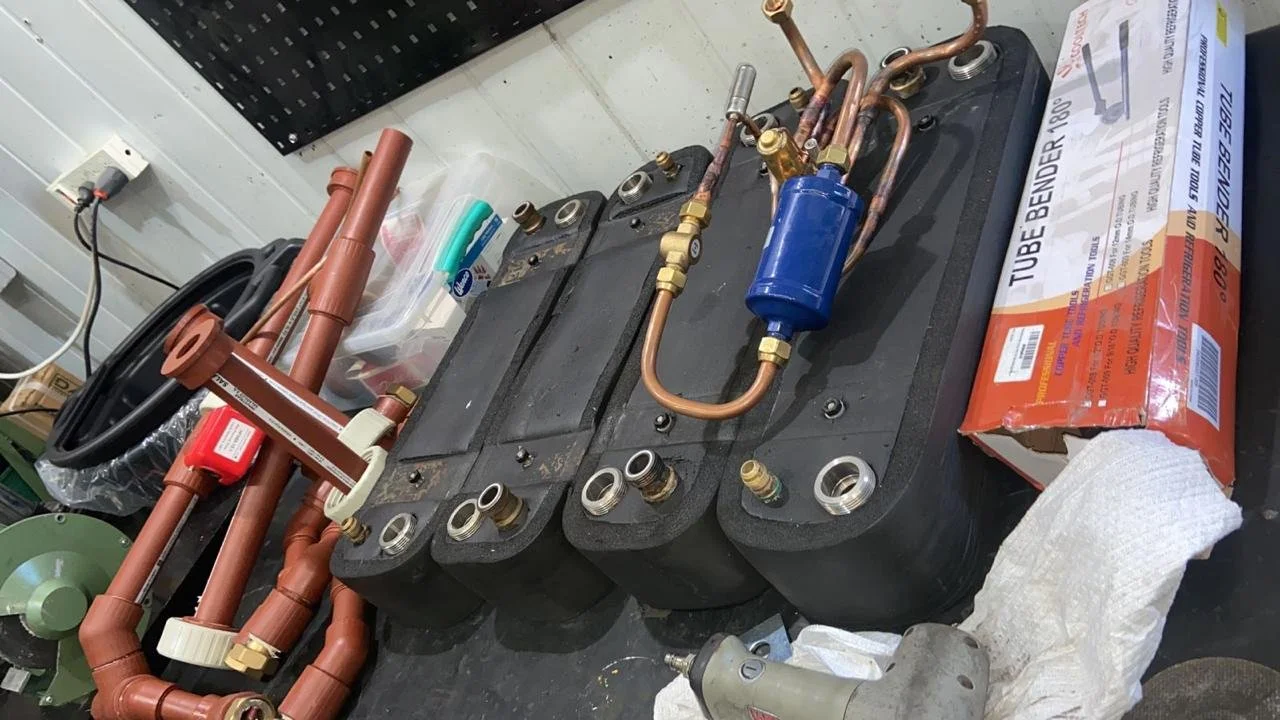 Componentes de un sistema de refrigeración o aire acondicionado en una mesa de trabajo, incluyendo tubos de cobre, unidades de control y accesorios.