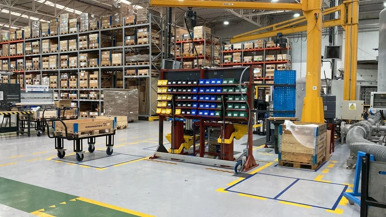 Interior de un almacén industrial con estanterías llenas de cajas de cartón, maquinaria y carretillas.