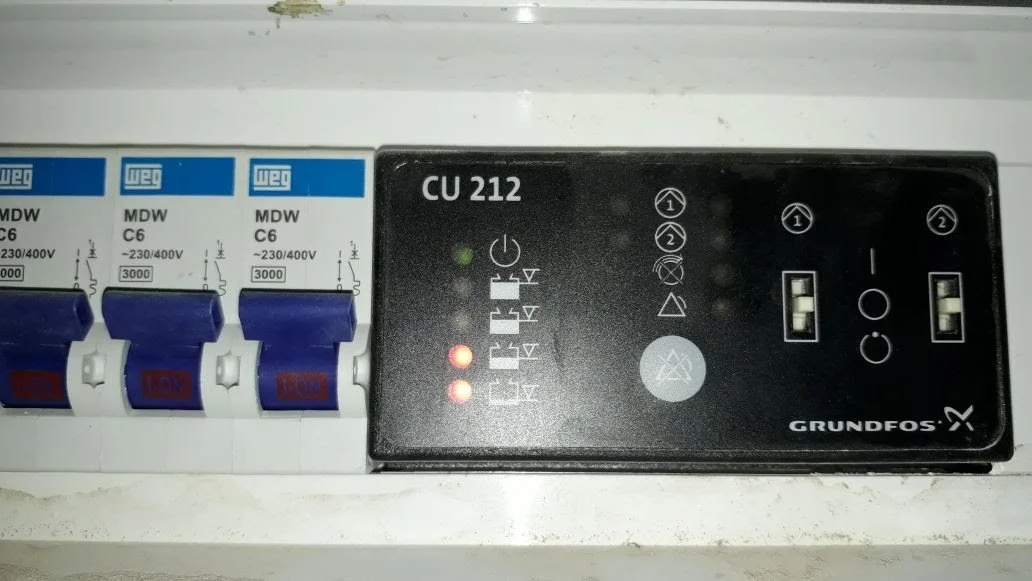 Tablero eléctrico con interruptores y un controlador Grundfos CU 212, con luces de advertencia encendidas.
