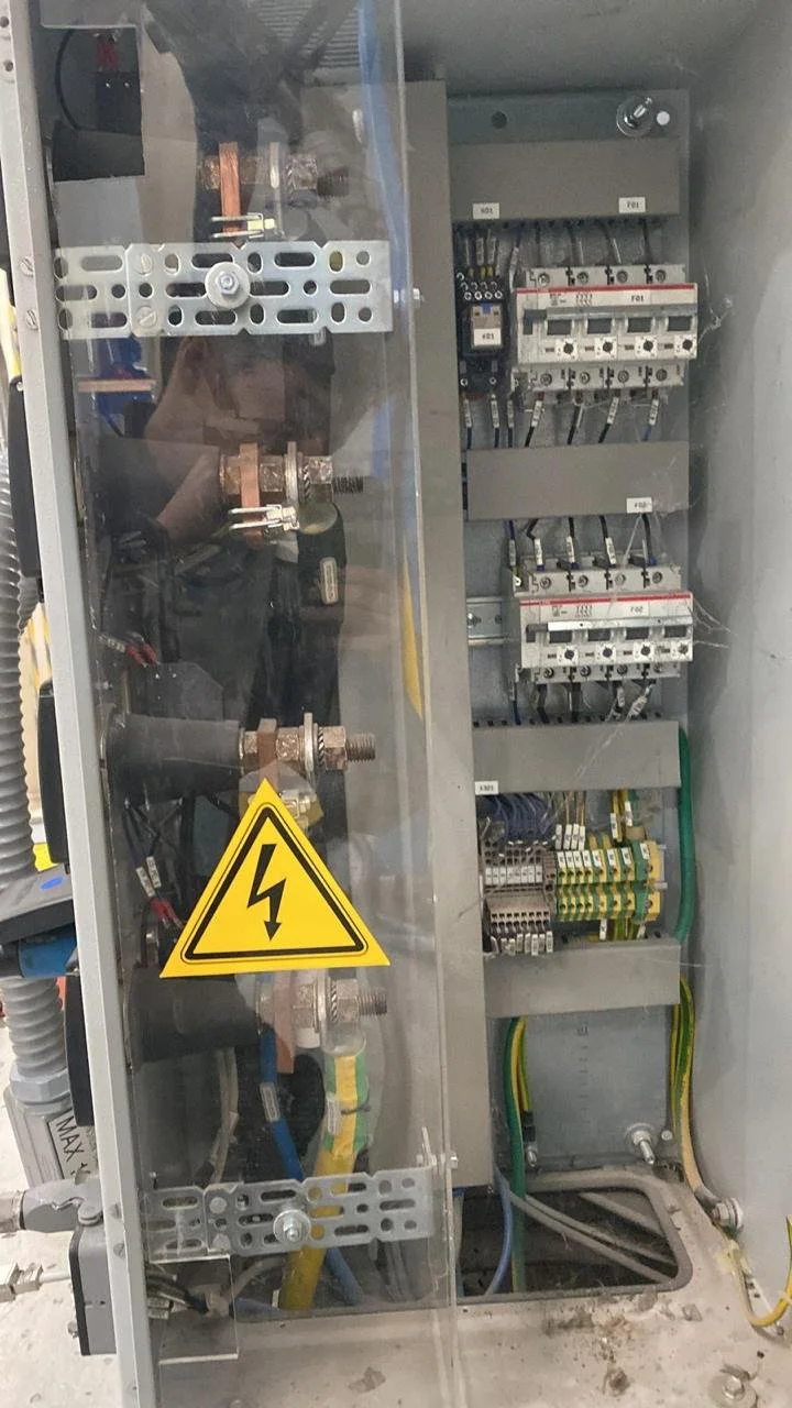 Panel eléctrico con componentes y cables internos, con señal de advertencia de alta tensión.