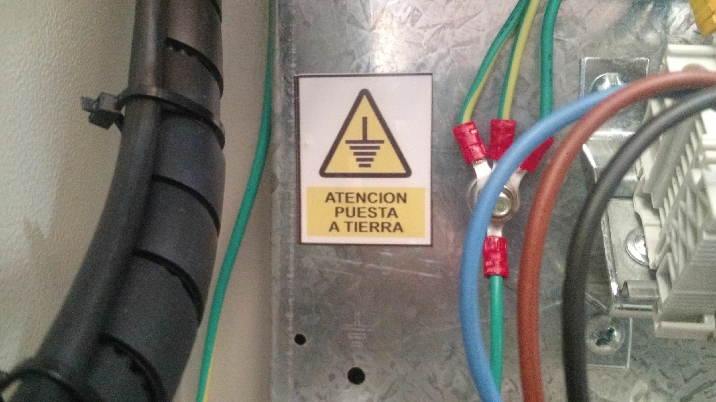 Advertencia de peligro en un panel con cables de colores y componentes eléctricos, que indica poner a tierra.