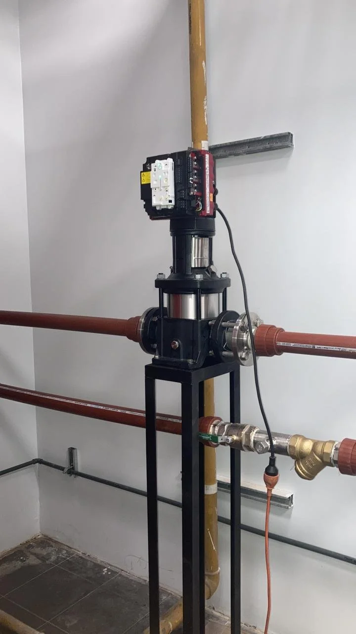 Sistema de bombeo de agua con tuberías de cobre, válvula y componentes eléctricos en una pared blanca.