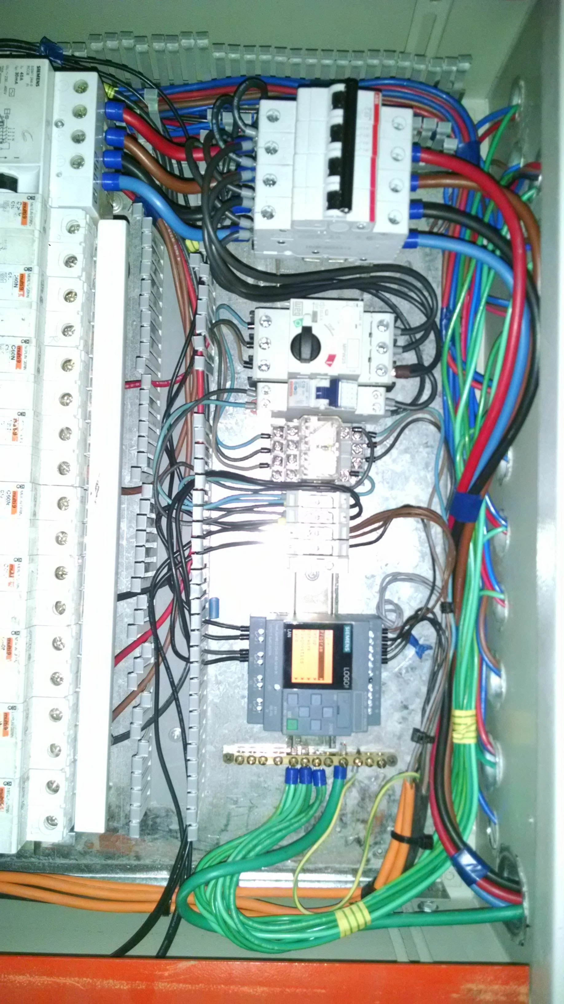 Cuadro eléctrico con componentes electrónicos, cables de diferentes colores y un controlador programable.