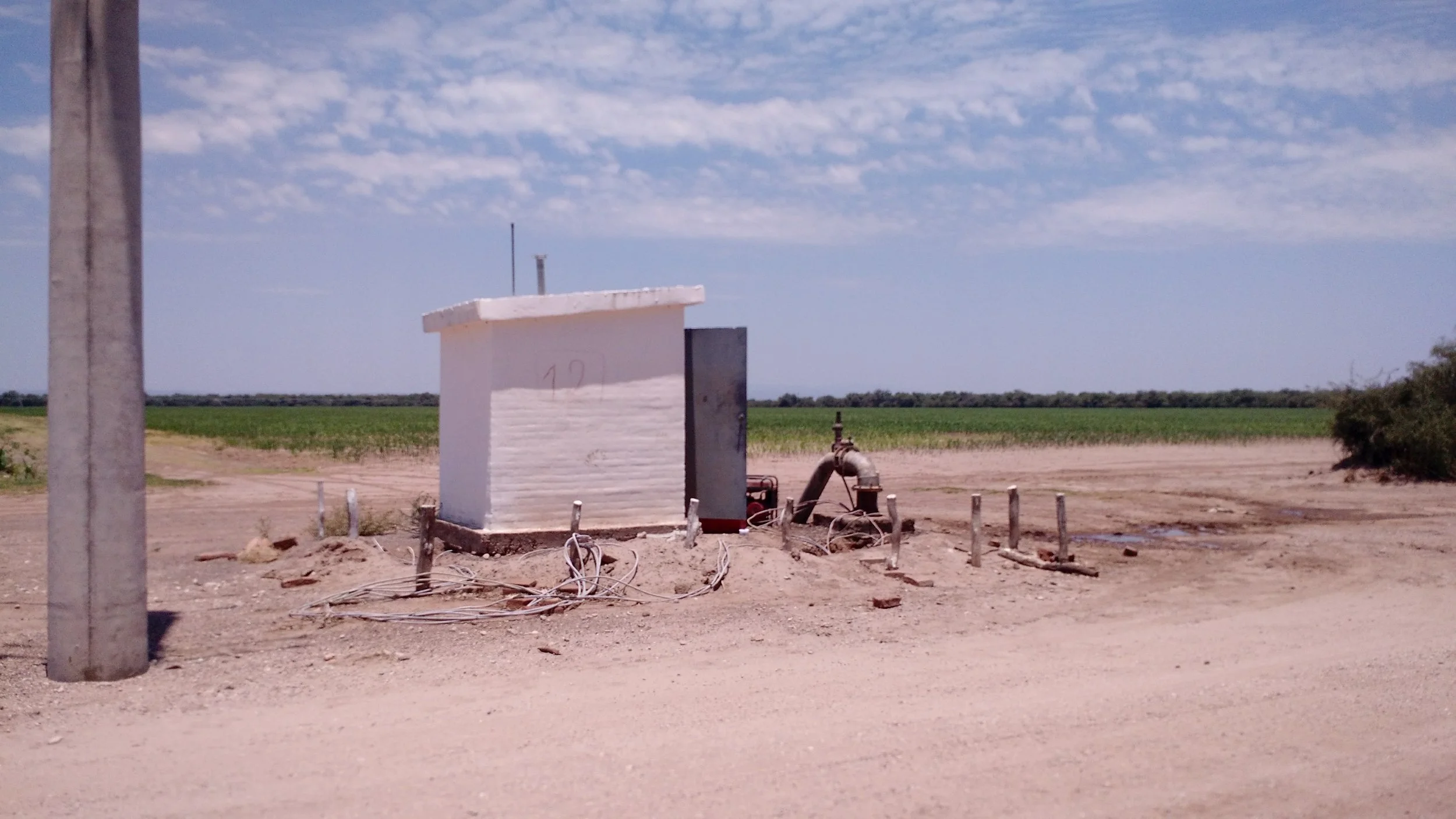 Estructuras y tuberías de agua frente a un campo agrícola con cielo despejado.