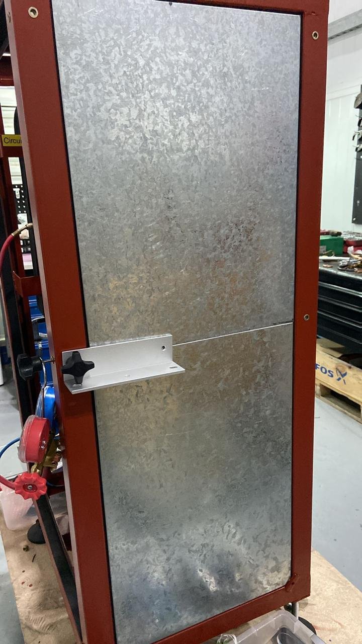 Equipo de fabricación con paneles metálicos y un tubo conectado con una válvula, situado sobre una mesa de trabajo en un taller.