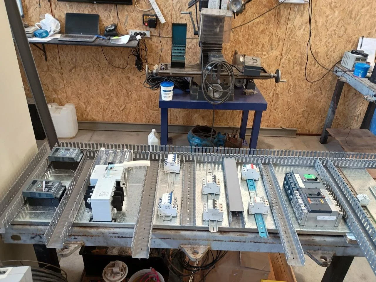 Mesa de trabajo con componentes eléctricos y un espacio de taller con herramientas y dispositivos electrónicos. Trabajo realizado para Mraz Service