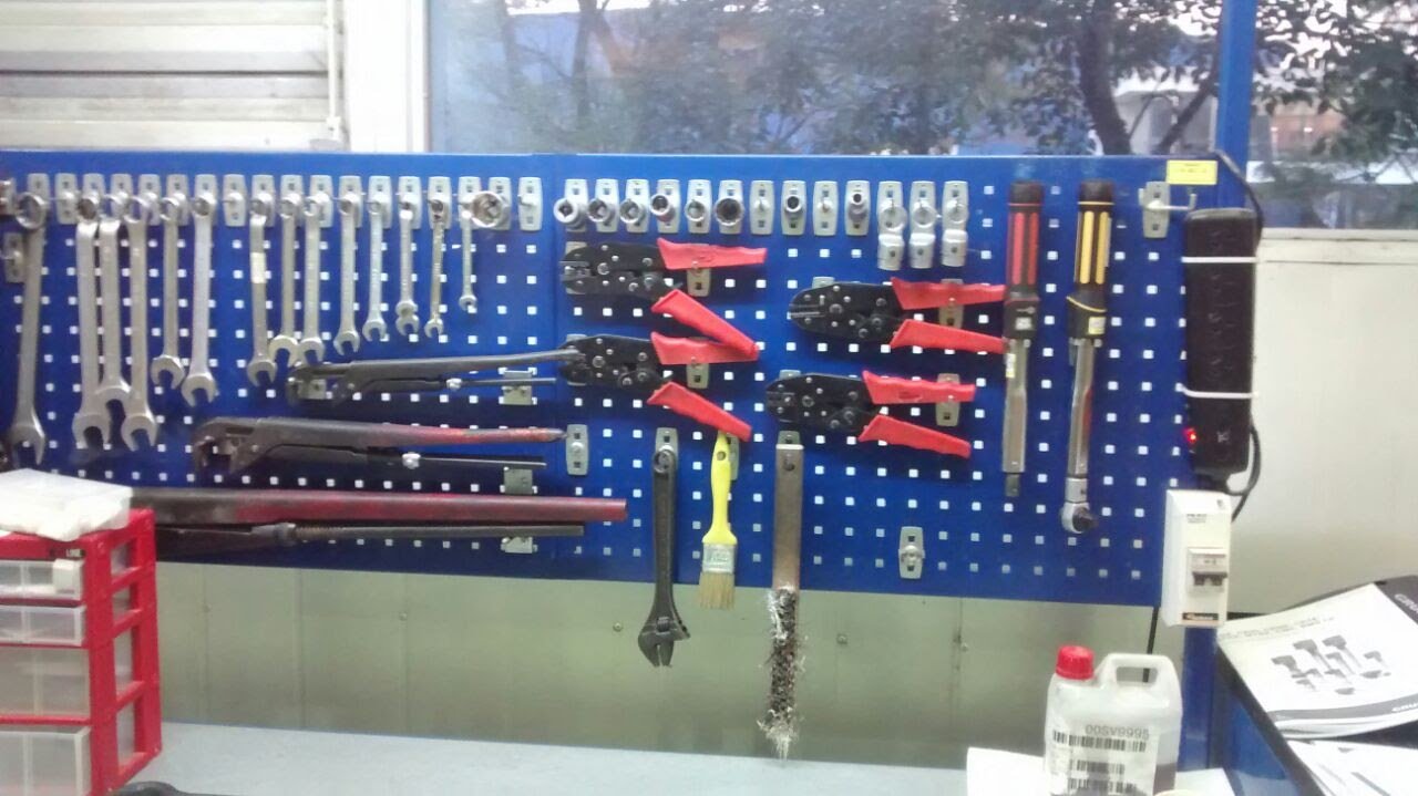 Perchero azul con herramientas de mecánica, incluyendo llaves, pinzas, destornilladores, una brocha y una llave inglesa, en un taller.