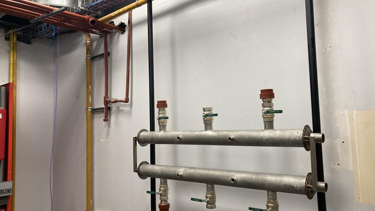 Sistema de tuberías metálicas horizontales y verticales en una pared, con válvulas y conexiones.