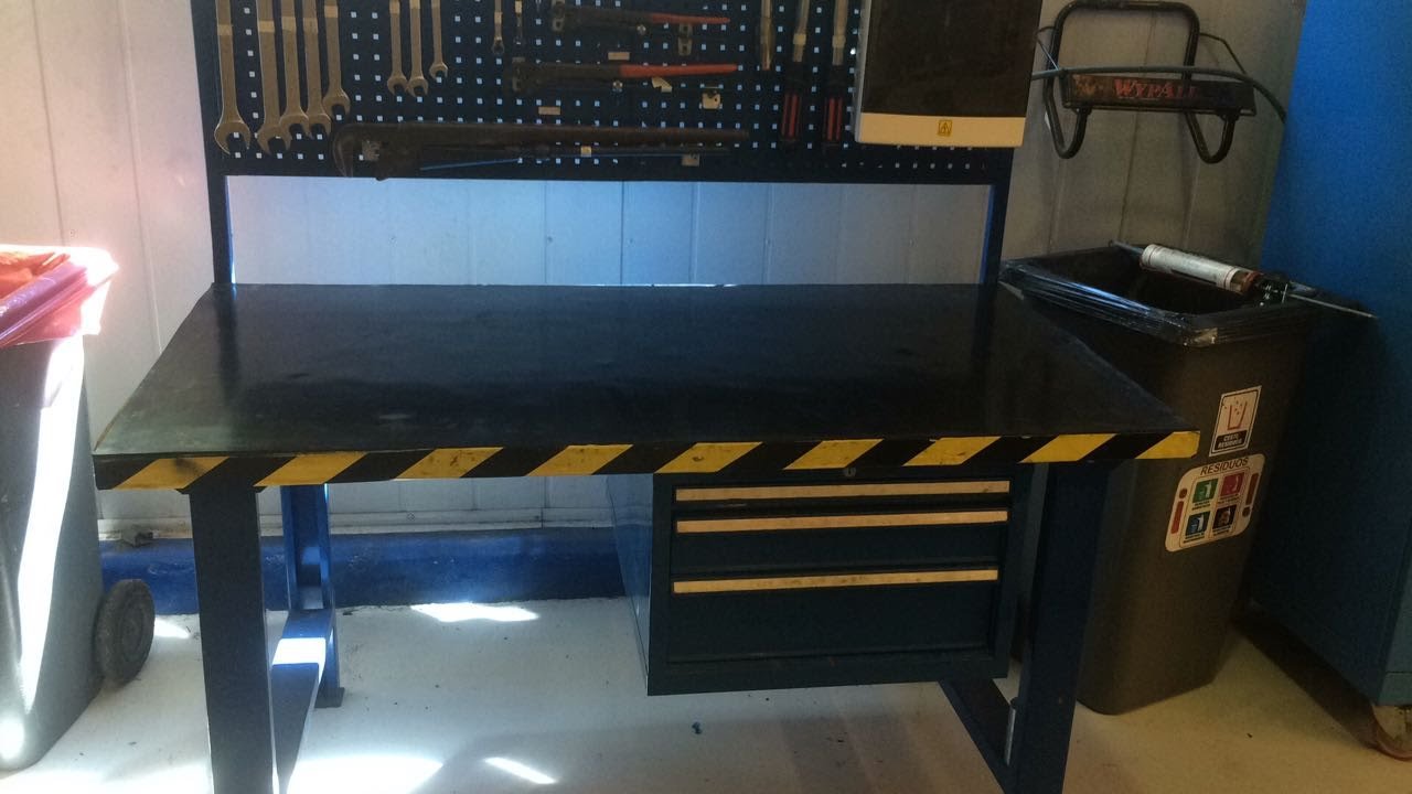 Un banco de trabajo en un taller de reparaciones con herramientas colgadas en un panel perforado y una caja de residuos en el lado derecho.