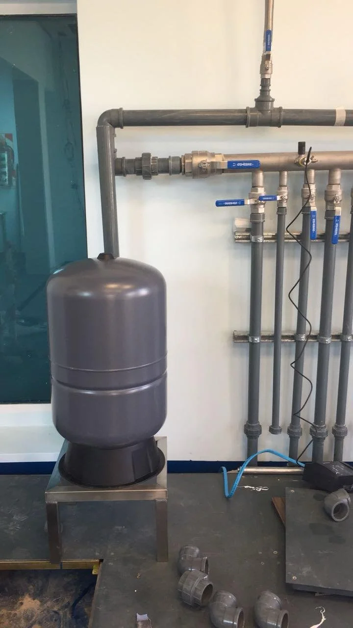 Sistema de tuberías de plomería con válvulas y un tanque, en un área de mantenimiento o técnico en construcción.