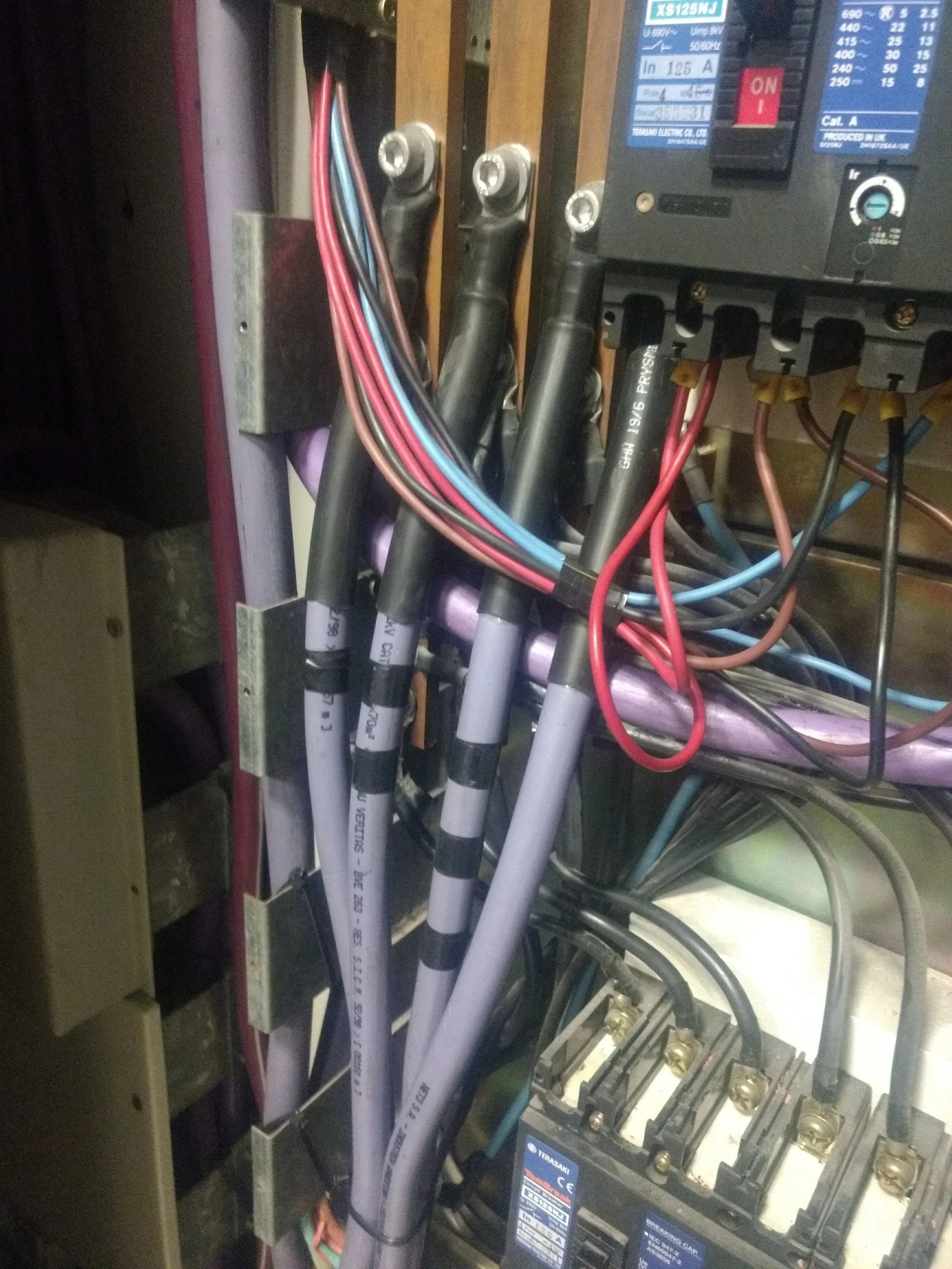 Vista interna de un panel eléctrico con cables de diferentes colores conectados a componentes y un interruptor en la esquina superior derecha.