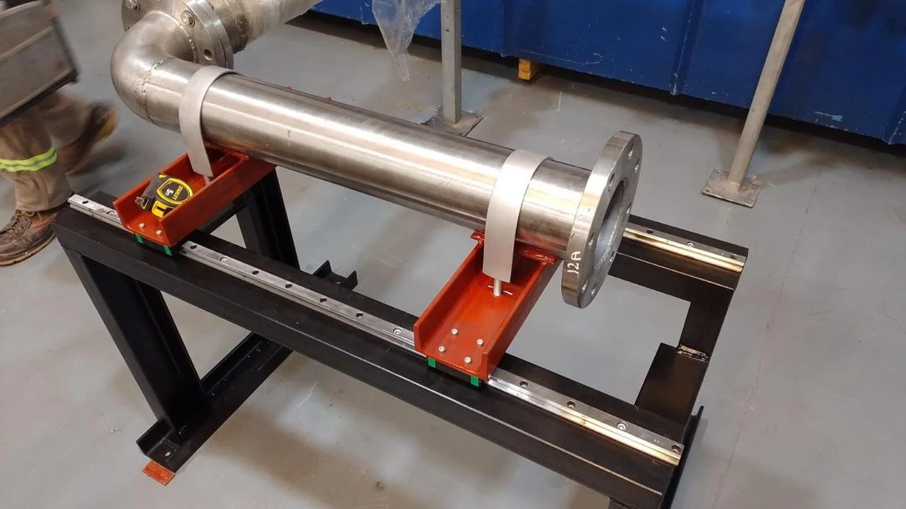 Tubo de metal grande colocado sobre una mesa de trabajo con instrumentos de medición, en un taller industrial.