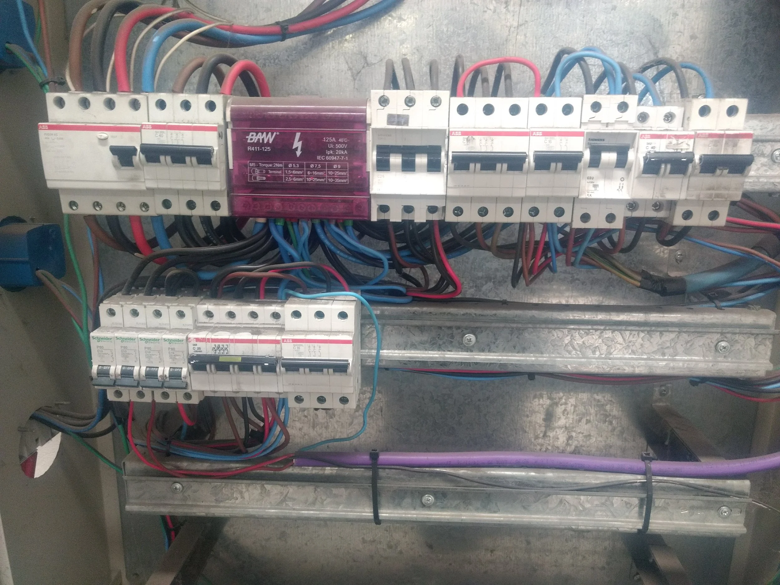 Pogas de distribución eléctrica con cables de diferentes colores y un interruptor en un panel metálico.