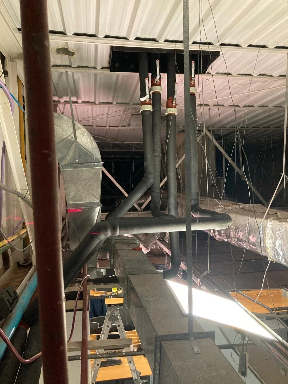 Tuberías negras, conductos de ventilación y estructura metálica en un techo industrial.