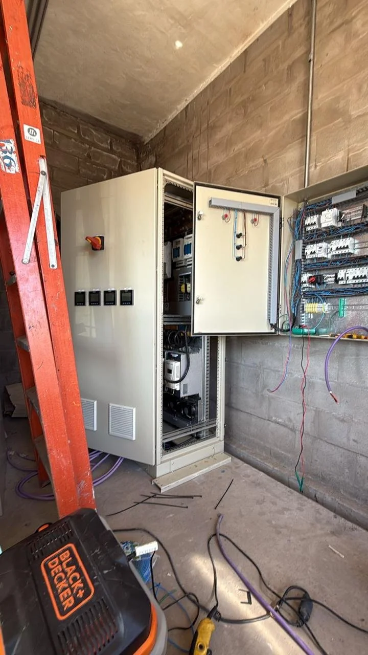 Cuadro eléctrico con puertas abiertas, cableado y herramientas en una construcción.