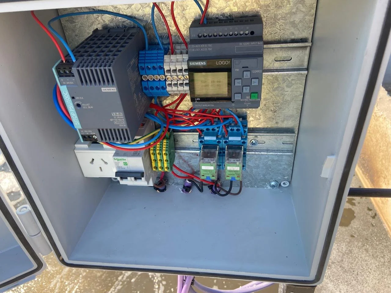 Cuadro de control eléctrico con componentes electrónicos y cableado, incluyendo un variador de frecuencia, relés y termostato, montado en una caja metálica de interior.