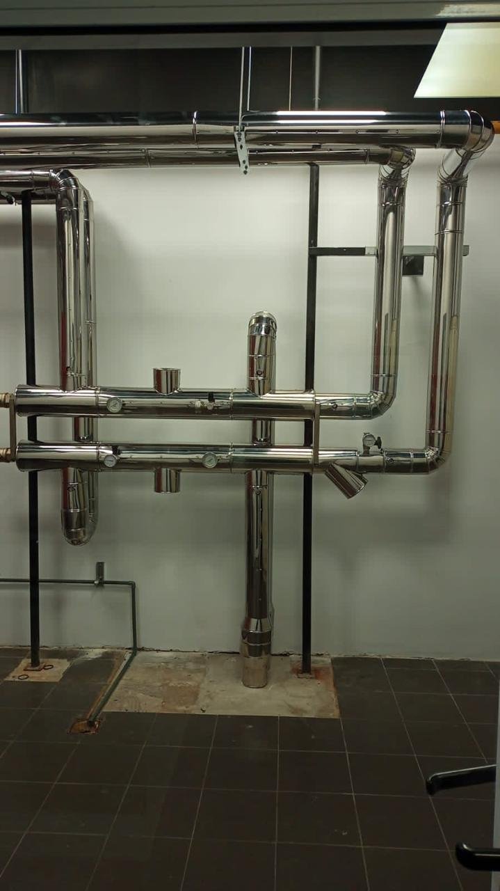 Tuberías de metal en una pared, con algunas conexiones y un soporte en un entorno industrial o de laboratorio.