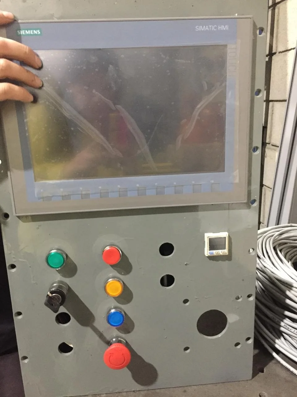 Panel de control con pantalla y botones de colores, en un ambiente industrial.
