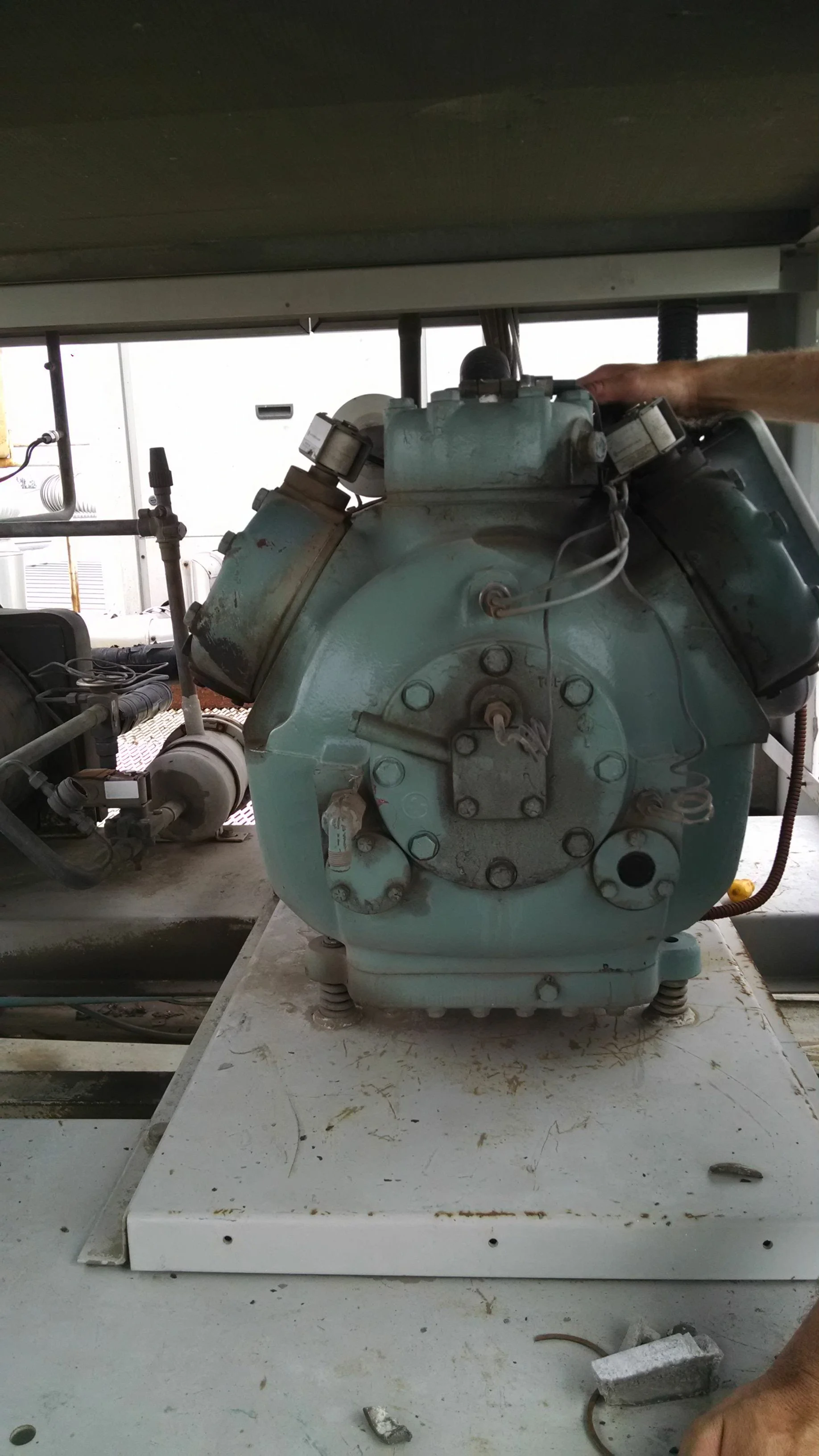 Maquinaria o equipo industrial sobre una mesa de trabajo, parece una bomba o motor grande con tornillos y tuberías conectadas