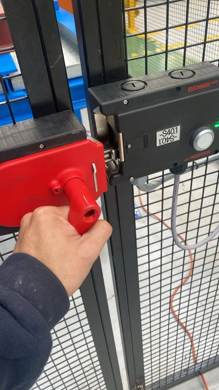 Persona operando un mecanismo de bloqueo en una puerta de malla metálica, usando una llave roja para activar el sistema.