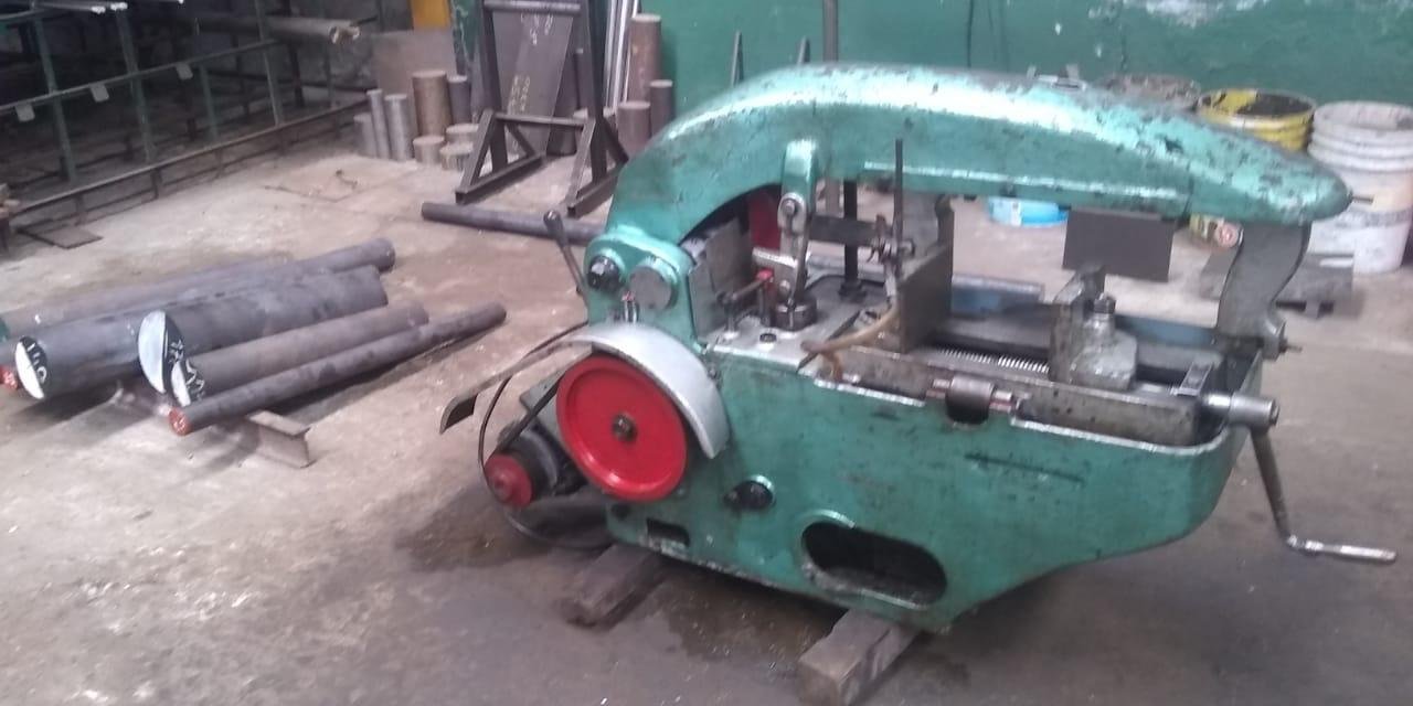 Una máquina de tornillo en un taller de metal, rodeada de barras de metal y herramientas de trabajo.