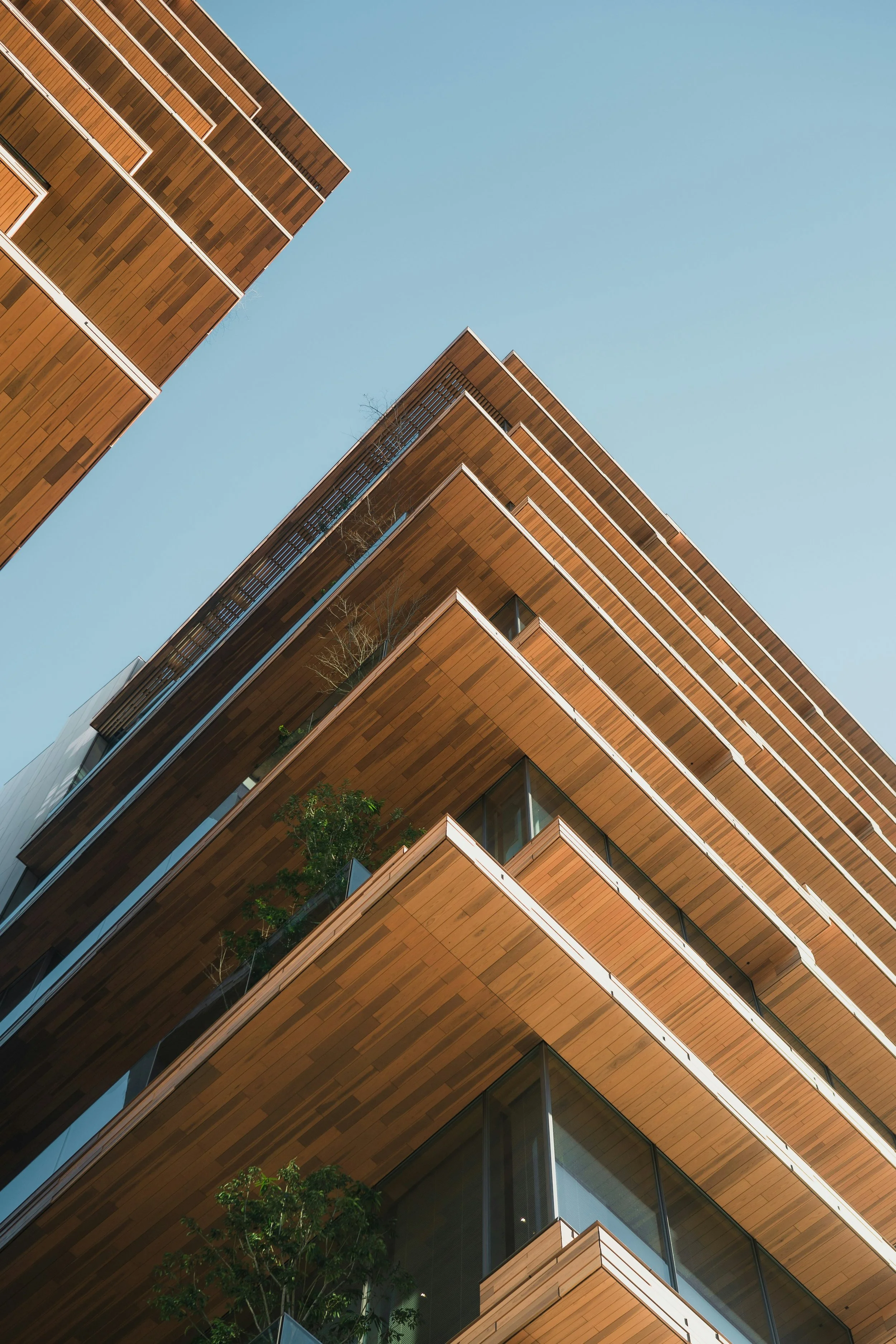 Low-angle view of modern building with wooden facade and glass balconies against clear blue sky.