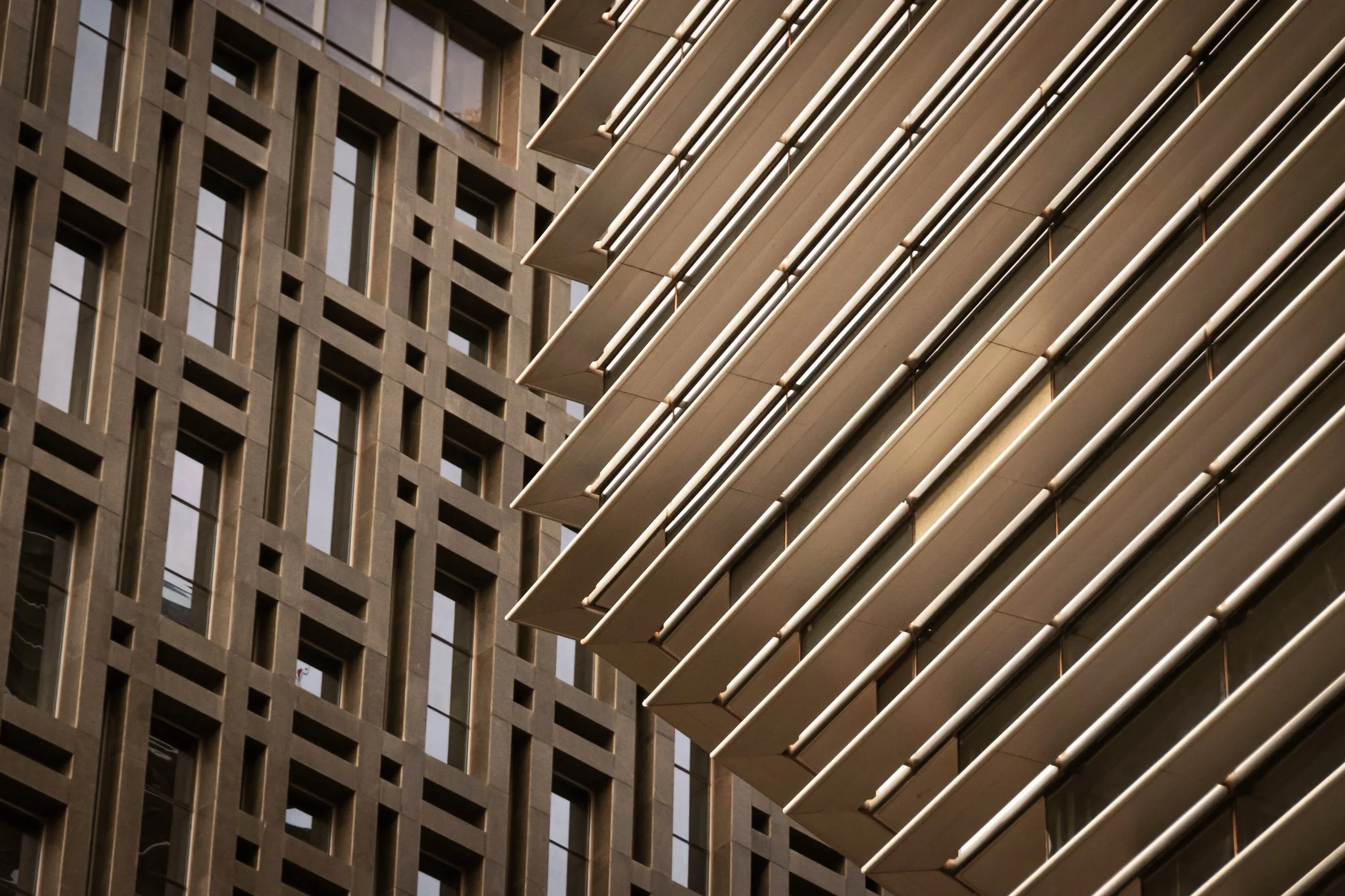Close-up view of the exterior of a modern building with a grid-like concrete facade and horizontal metal louvers.