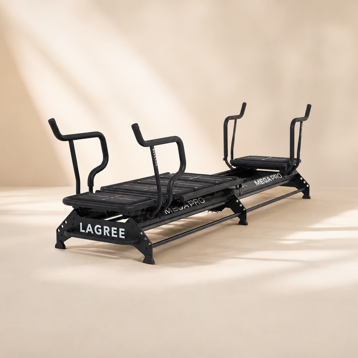 A black reformer with handlebars for different pushing and pulling exercises, labeled with brand names Lagree and Mega Pro, placed on a beige floor against a plain beige wall.