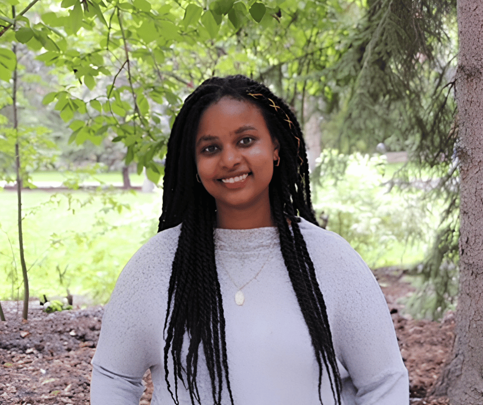 young woman with black braided hair smiling and standing in nature