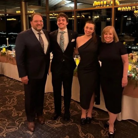 Two young adults and two adults, dressed in formal attire standing together at a banquet or celebration.