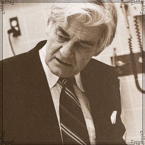 A black and white photo of an older man with gray hair, wearing a suit and tie, looking down.